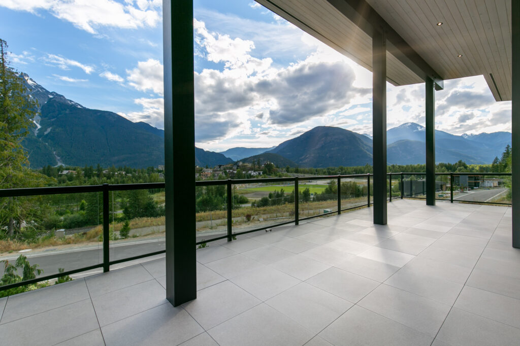 Covered deck with forest views Open living space featuring large glass doors leading to a covered deck with forest views
