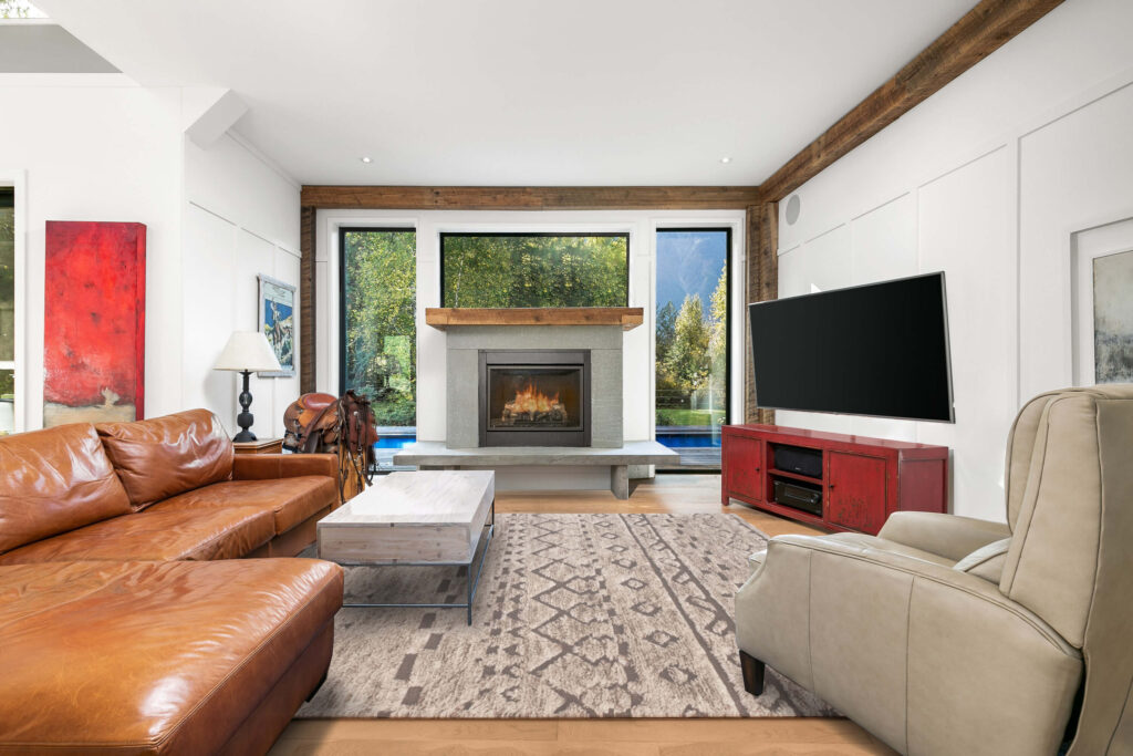 Living room with fireplace, wood beam ceiling, and forest views